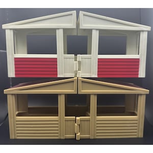 May include: A toy stable structure consisting of two levels. The top level features white frames with red horizontal siding. The bottom level is tan with horizontal siding and includes hinged doors. The structure is modular with open stalls.