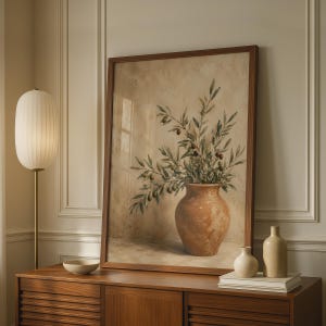 May include: A framed wall art print featuring a still life painting of an olive branch with small green and dark olives inside a rounded terracotta-coloured vase. The artwork has a neutral, textured beige background and a dark brown wooden frame.