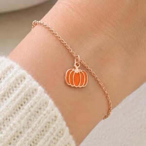 Op de afbeelding: Een delicate roségouden kettingarmband met een kleine, feloranje geëmailleerde pompoenbedel. De bedel hangt aan een eenvoudige schakelketting en heeft een heldere oranje kleur met roségouden omlijningen voor een subtiel accent.