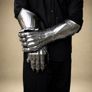 May include: A pair of polished steel gauntlets featuring articulated finger plates and intricate etched scrollwork patterns. The metal armor covers the hands and forearms, showcasing a reflective silver finish with detailed craftsmanship.
