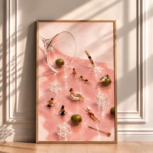 Op de afbeelding: Een ingelijste kunstdruk met een omgevallen martiniglas op een roze ondergrond, waarin miniatuurfiguurtjes in de vloeistof zwemmen. De scène bevat groene olijven, doorzichtige ijsblokjes en een cocktailprikker in een surrealistische setting.