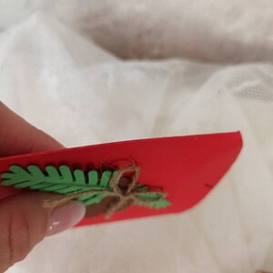 Peut inclure: Une carte rouge avec une feuille de feutre verte et un n&oelig;ud en ficelle brune. La feuille est attach&eacute;e &agrave; la carte avec un gland en feutre brun.
