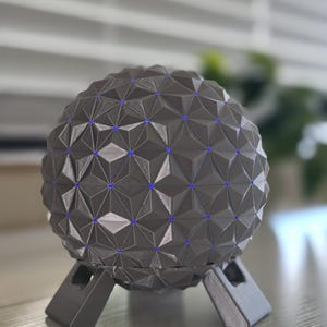 Puede incluir: Un objeto esférico con un patrón geodésico geométrico compuesto por paneles triangulares de color gris oscuro. Pequeñas luces LED de color azul brillante están incrustadas en los puntos de intersección de los triángulos.