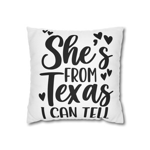 Może przedstawiać: Kwadratowa biała poduszka dekoracyjna z czarnym napisem "She's FROM Texas I CAN TELL" wykonanym mieszanką pisma odręcznego i drukowanego. Wzór jest ozdobiony kilkoma małymi czarnymi ikonami serc rozmieszczonymi wokół słów.