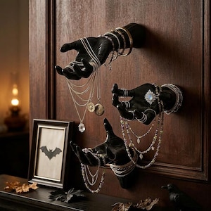 Può includere: Tre sculture di mani nere montate a parete su una superficie in legno, che espongono vari gioielli tra cui collane a strati, braccialetti di perline e anelli. Le mani sono posizionate in modo da sostenere e mettere in mostra gli accessori.