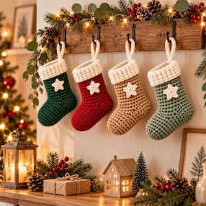 May include: Four crocheted Christmas stockings hanging from a wooden rack. Each stocking features a thick cream-colored cuff and a small crocheted star appliqué. The stockings are colored dark green, deep red, tan, and sage green respectively.