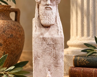 May include: A stone-coloured herm sculpture featuring a bearded male head with a textured cap and long hair, set atop a rectangular pillar base. The surface has a weathered, matte finish with subtle brown highlights, depicting a classical bust.
