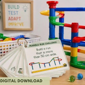 May include: A set of laminated challenge cards on a metal ring, featuring the text MARBLE RUN CHALLENGE and Build a run that is more than 50 cm wide, alongside a colourful plastic marble run construction set with blue, red, yellow, and green tracks.
