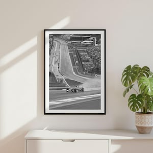 Puede incluir: Una impresión de arte mural enmarcada en blanco y negro que representa un coche de Fórmula 1 en un circuito. El coche está situado en una curva con una tribuna llena de espectadores al fondo. La palabra Vodafone es visible en la señalización.