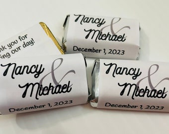 May include: Three white chocolate bar wrappers with a silver foil accent. The wrappers have a black and gray design with the text "Nancy & Michael" and "December 1, 2023". One wrapper has the text "Thank you for sharing our day!"