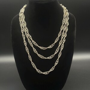 May include: A multi-strand silver-toned necklace featuring a delicate twisted chain design. The necklace consists of three distinct layers of interconnected metallic links that drape in a cascading formation, creating a textured appearance.
