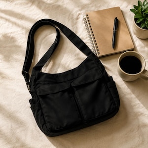 May include: A black crossbody bag featuring a long adjustable shoulder strap, two front flap pockets, and side pockets. The bag is constructed from a solid black fabric and includes a main zippered compartment with a flap closure over the front pockets.