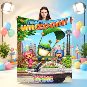 May include: A rectangular fleece blanket featuring the Team Umizoomi logo, characters Milli, Geo, and Bot in a city park setting with a fountain, and a customizable name section at the bottom, all rendered in vibrant colors against a blue sky.
