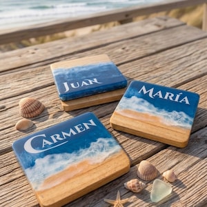 Puede incluir: Tres posavasos cuadrados de madera con un diseño de olas oceánicas en resina, que incluyen espuma blanca y detalles de orilla arenosa. Cada posavasos está personalizado con los nombres Juan, María y Carmen en blanco, junto a varias conchas.