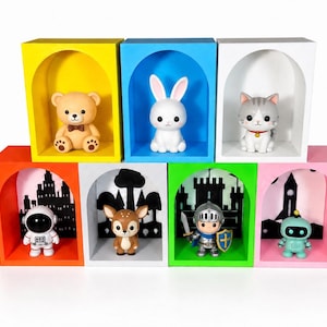 Könnte beinhalten: Ein Set aus sieben bunten, bogenförmigen Regalfächern in zwei Reihen. Die obere Reihe zeigt ein gelbes Fach mit einem Teddybären, ein blaues mit einem weißen Kaninchen und ein weißes mit einer Katze. Die untere Reihe enthält ein oranges Fach mit einem Astronauten, ein graues mit einem Reh, ein grünes mit einem Ritter und ein rosa Fach mit einem Roboter.