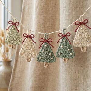 Peut inclure: Une guirlande composée de cinq décorations de sapin de Noël au crochet suspendues à une ficelle blanche. Les sapins alternent entre le vert sauge et le crème, ornés de petites perles blanches et d'un nœud en fil rouge foncé.