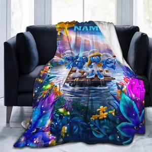 May include: A soft throw blanket featuring a vibrant, colorful illustration of three Smurf characters standing on a wooden raft in a river. The scene includes lush, glowing tropical foliage, a waterfall in the background, and the text NAM at the top.