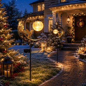 May include: Two solar garden stakes featuring a crescent moon frame with star cutouts and a hummingbird figure. Each stake holds a glowing, spherical crackle glass light bulb suspended from the moon, mounted on a thin black metal pole.