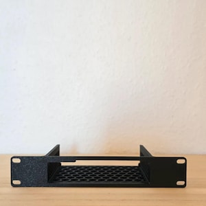 May include: A black rack-mount bracket featuring a flat front panel with two mounting holes on each side and a central rectangular cutout. The base of the bracket consists of a rigid, black hexagonal honeycomb grid pattern for ventilation.