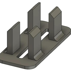 May include: A gray rectangular plastic component featuring a flat base with rounded corners and four vertical, upright prongs. Each prong has a beveled top edge and is integrated into the base, which contains two elongated rectangular slots.