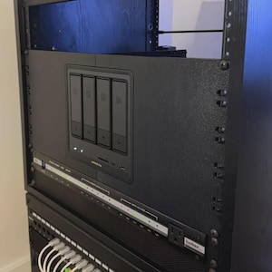 Puede incluir: Una unidad de distribución de energía negra montada en rack con cuatro interruptores numerados del 01 al 04, un puerto USB pequeño y luces indicadoras de estado. Debajo, una regleta horizontal con varios indicadores LED y un enchufe.