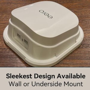 May include: A white plastic mounting bracket for an eero router, featuring a square base with rounded corners and a recessed center. The text "Sleekest Design Available Wall or Underside Mount" is printed in black on a light beige background below.