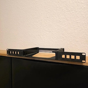May include: A black rack-mount shelf featuring a flat base and a front panel with four rectangular ventilation slots on each side. The metal component includes mounting holes at both ends for secure installation into a standard server rack frame.
