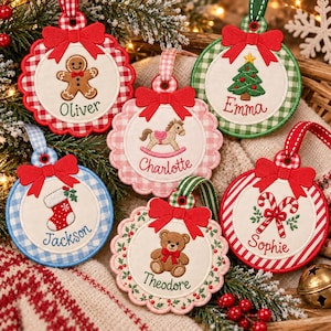 May include: Six round fabric Christmas ornaments featuring embroidered designs including a gingerbread man, rocking horse, Christmas tree, stocking, teddy bear, and candy canes. Each ornament has a red bow and a name embroidered in cursive.