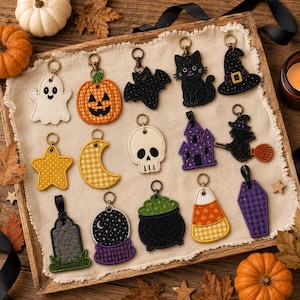 May include: A collection of fourteen embroidered Halloween-themed keychains featuring a ghost, pumpkin, bat, black cat, witch hat, star, crescent moon, skull, haunted house, witch on a broom, tombstone, crystal ball, cauldron, candy corn, and coffin.