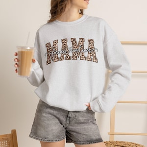 May include: A light grey crewneck sweatshirt featuring the word MAMA in large block letters with a brown and black leopard print pattern. The cursive text forever and ever is layered over the centre of the word MAMA in white script.