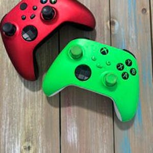May include: Two wireless video game controllers, one in a metallic red finish and the other in a bright neon green finish. Both controllers feature black analog sticks, a directional pad, and standard action buttons labeled with A, B, X, and Y.