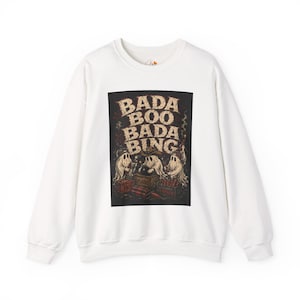 May include: A white long-sleeve sweatshirt featuring a central rectangular graphic on the chest. The graphic depicts three ghosts wearing hats, surrounded by crates of explosives, with the text BADA BOO BADA BING printed in a distressed font.