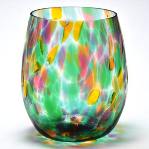 May include: A green glass wine glass with a colorful, speckled pattern. The glass has a round, wide base and a slightly flared rim.