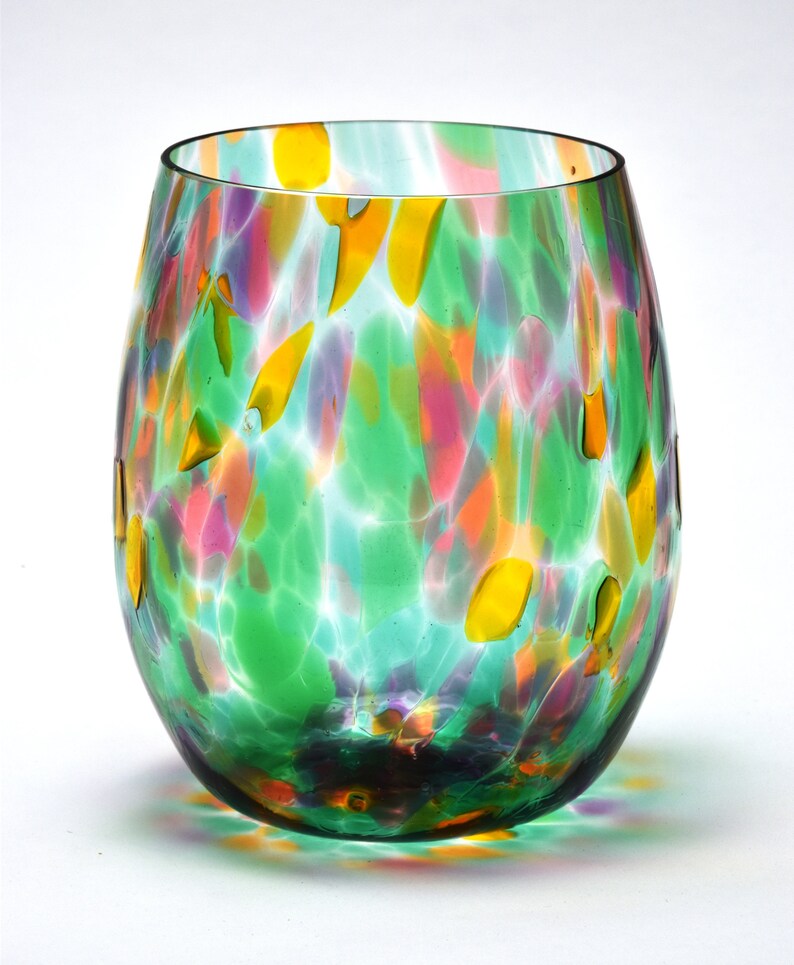 May include: A green glass wine glass with a colorful, speckled pattern. The glass has a round, wide base and a slightly flared rim.