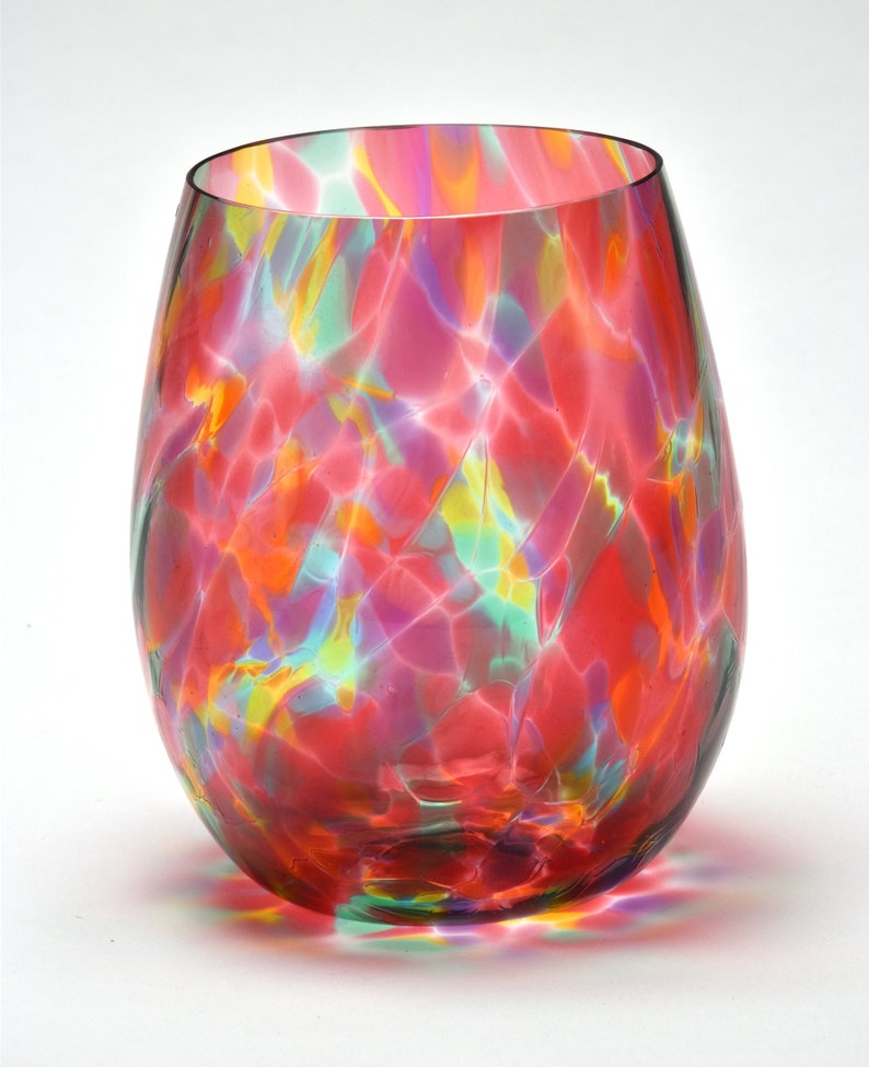 May include: A colorful glass wine glass with a swirling pattern of red, pink, green, and yellow. The glass has a rounded bottom and a wide opening.