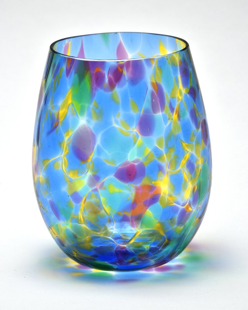 May include: A blue glass wine glass with a colorful, marbled pattern. The glass has a round, wide base and a narrow opening.