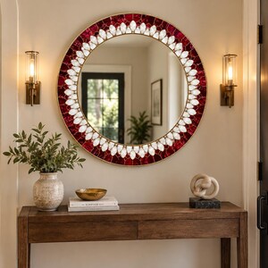 May include: A round wall mirror featuring a decorative frame composed of deep red, faceted glass pieces arranged in a mosaic pattern, accented by an inner ring of white, petal-shaped glass elements that create a bright, floral-inspired border.
