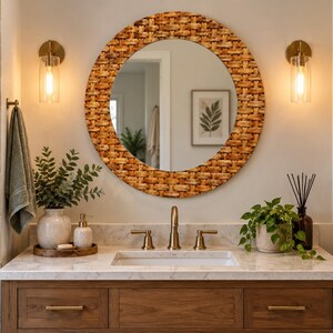 May include: A round wall mirror with a woven light brown rattan frame positioned above a bathroom vanity. The vanity features a white marble countertop, a brass faucet, and a wooden cabinet with brass handles, complemented by two wall sconces.