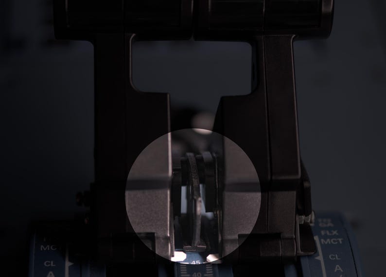 May include: A black aircraft throttle quadrant featuring two vertical levers with a central circular highlight. The base displays printed text including FLX, MCT, and CL, with a numerical scale visible at the bottom centre of the control unit.