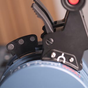 May include: A black throttle quadrant lever assembly featuring a red button on top, a white arch symbol, and three circular silver magnets on a small black attachment. The base is a light blue curved housing with white markings and red text.