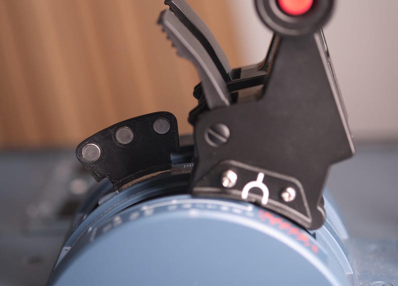 May include: A black throttle quadrant lever assembly featuring a red button on top, a white arch symbol, and three circular silver magnets on a small black attachment. The base is a light blue curved housing with white markings and red text.