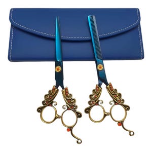 Puede incluir: Un par de tijeras de corte y tijeras de entresacar de metal azul con mangos dorados ornamentados decorados con pequeños cristales naranjas, acompañadas de un estuche rectangular azul con costuras blancas en los bordes.