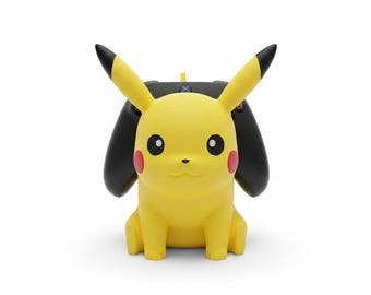 Puede incluir: Un soporte para mando en forma de Pikachu amarillo con orejas largas de puntas negras, mejillas circulares rojas y ojos negros. El soporte está diseñado para sostener un mando de juego negro, que es parcialmente visible detrás de la figura.