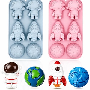 May include: Two rectangular silicone molds in light blue and pink, each featuring six cavities shaped like astronauts, rockets, and globes. Below the molds are four individual finished figures: a white astronaut, a green and blue globe, a red and white rocket, and a blue globe.