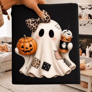 Peut inclure: Un carré de tissu noir orné d'une applique de fantôme blanc avec un nœud à motif léopard, tenant une citrouille orange et un gobelet en plastique avec un manchon noir affichant une icône de fantôme blanc. Le fantôme présente des pièces en tissu.