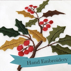 Könnte beinhalten: Handgestickte Stechpalmenzweig mit grünen, goldenen und braunen Blättern und roten Beeren. Die Stickerei ist auf einem weißen Stoffhintergrund. Der Text "Handstickerei" befindet sich auf einem blauen Band.