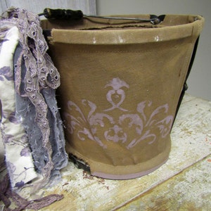 May include: A brown canvas bucket with a wire handle and a floral design. The bucket is sitting on a wooden surface.