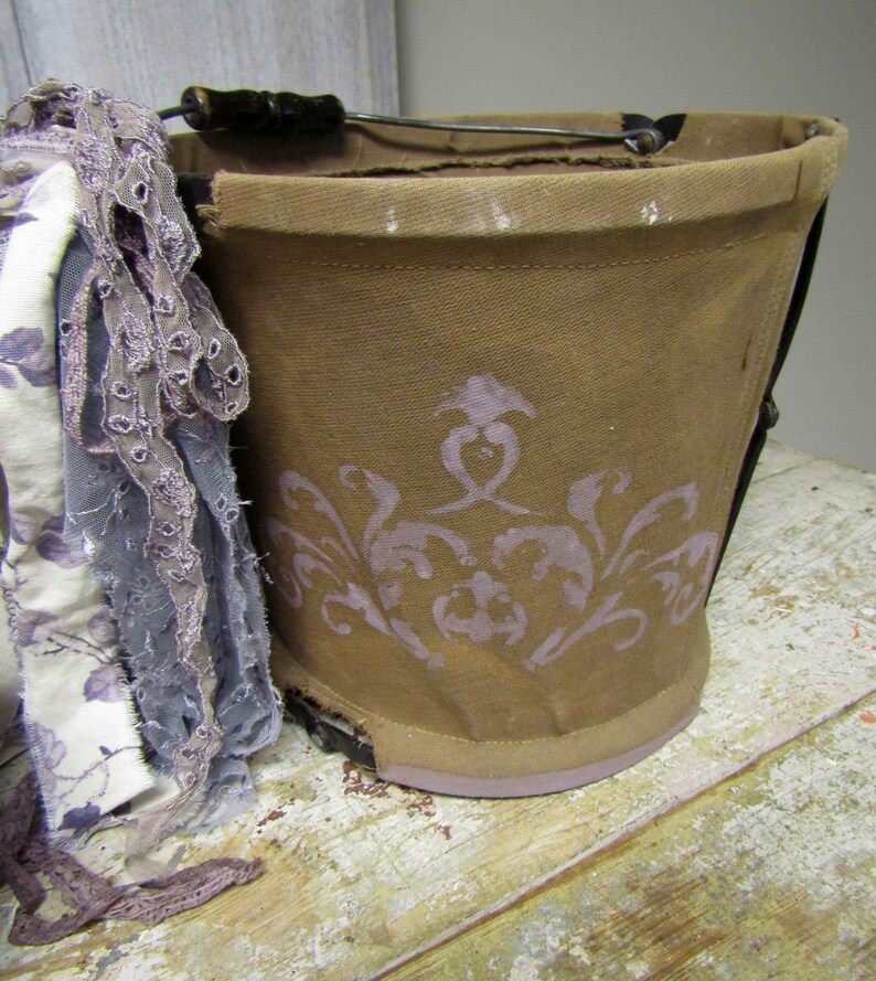 May include: A brown canvas bucket with a wire handle and a floral design. The bucket is sitting on a wooden surface.