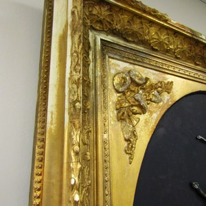 Puede incluir: Un marco de imagen de color dorado adornado con tallas intrincadas y un fondo negro. El marco tiene un acabado desgastado con pintura blanca que se ve a trav&eacute;s.