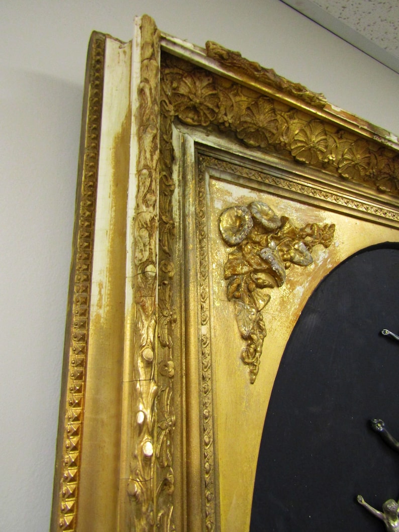 Puede incluir: Un marco de imagen de color dorado adornado con tallas intrincadas y un fondo negro. El marco tiene un acabado desgastado con pintura blanca que se ve a trav&eacute;s.